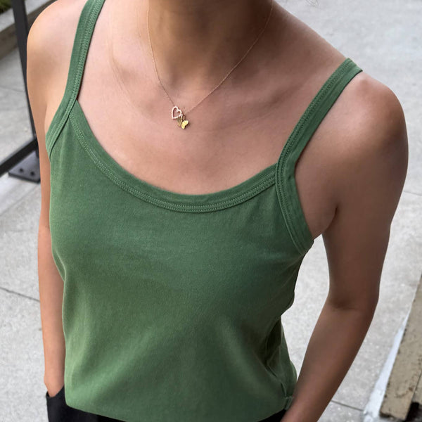 Person wearing a green tank top and black pants on a sidewalk.