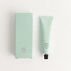 Mint green tube and packaging of Corpus hand lotion on a white background