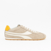 A beige suede low-top sneaker with white leather side stripes, white laces, a yellow heel tab, and a gum sole, shown in profile against a plain white background.