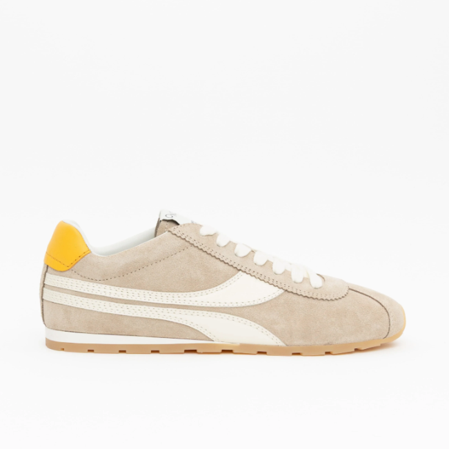 A beige suede low-top sneaker with white leather side stripes, white laces, a yellow heel tab, and a gum sole, shown in profile against a plain white background.