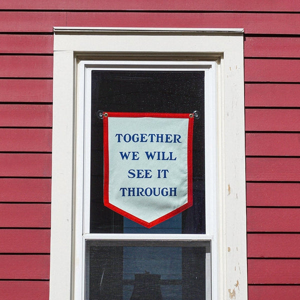 Window with a banner reading 'Together we will see it through' on a red building.
