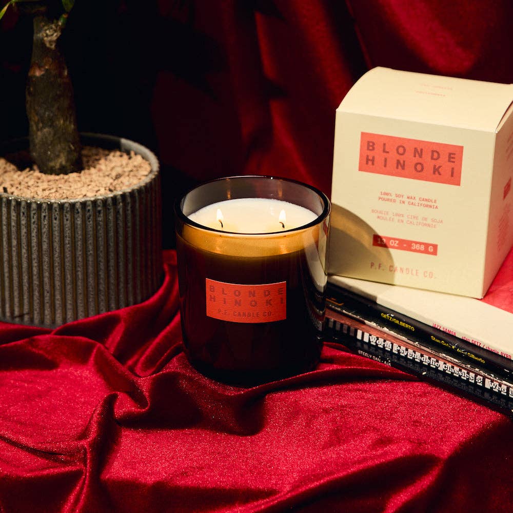 Candle with 'Blonde Hinoki' packaging on a red surface