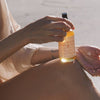 Person applying High Noon Body Oil to their arm with a blurred background