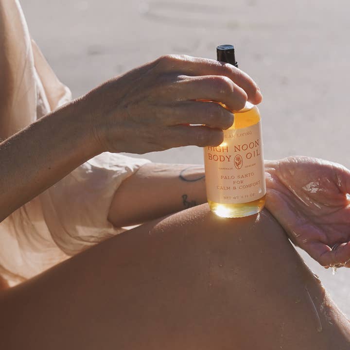 Person applying High Noon Body Oil to their arm with a blurred background