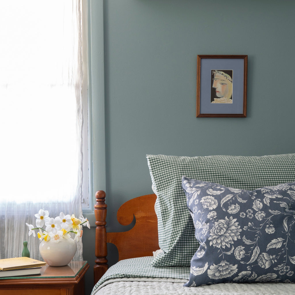 Bedroom with wooden headboard, floral and checkered pillows, and a framed Picasso portrait on the wall.