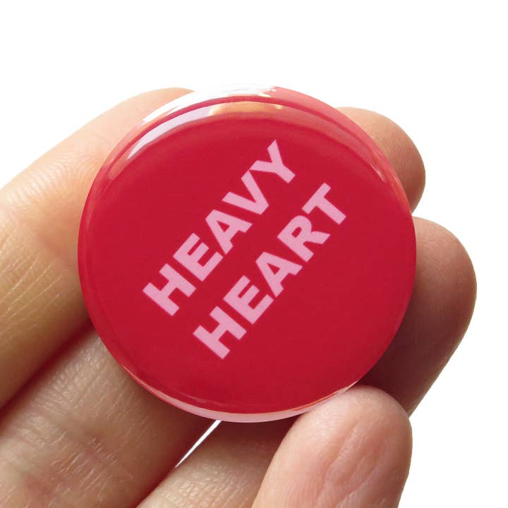 Red button with 'HEAVY HEART' text held in a hand against a white background