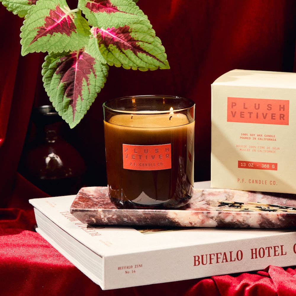 Candle with 'Plush Vetiver' packaging on a book, surrounded by decorative elements.