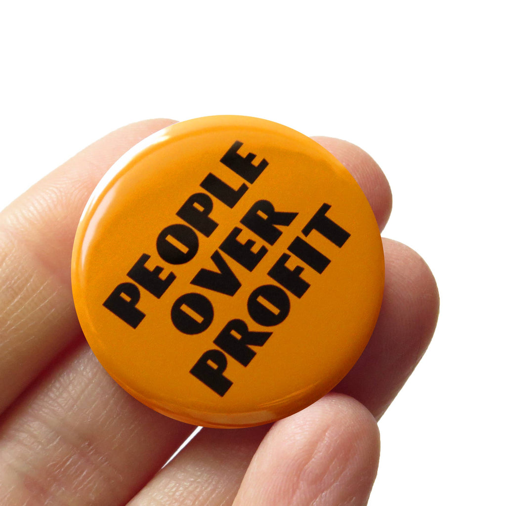 Orange button with 'People Over Profit' text held in a hand against a white background