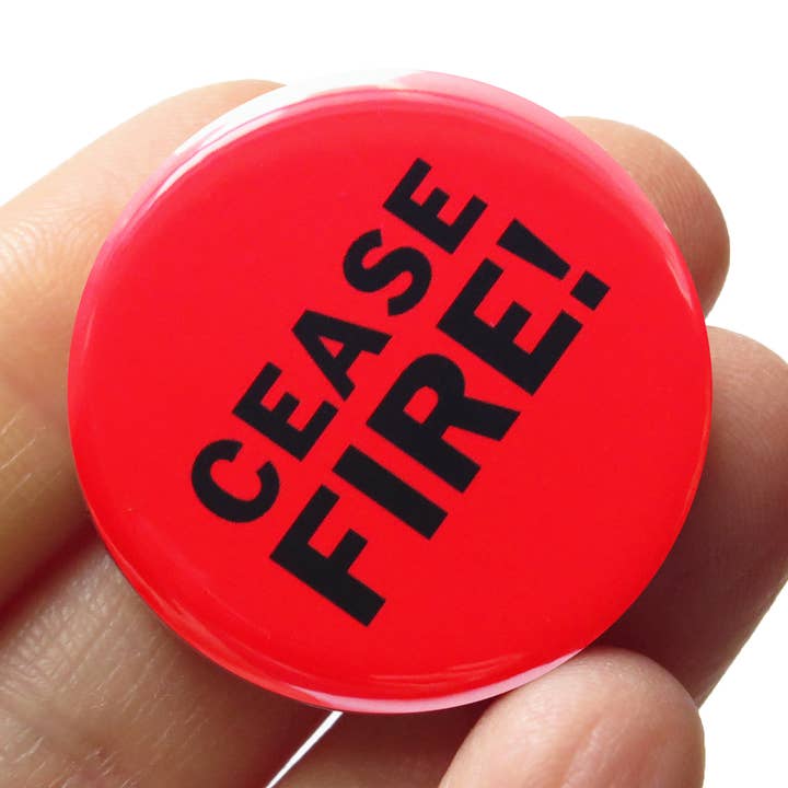 Red pin button with 'CEASE FIRE!' text held in a hand