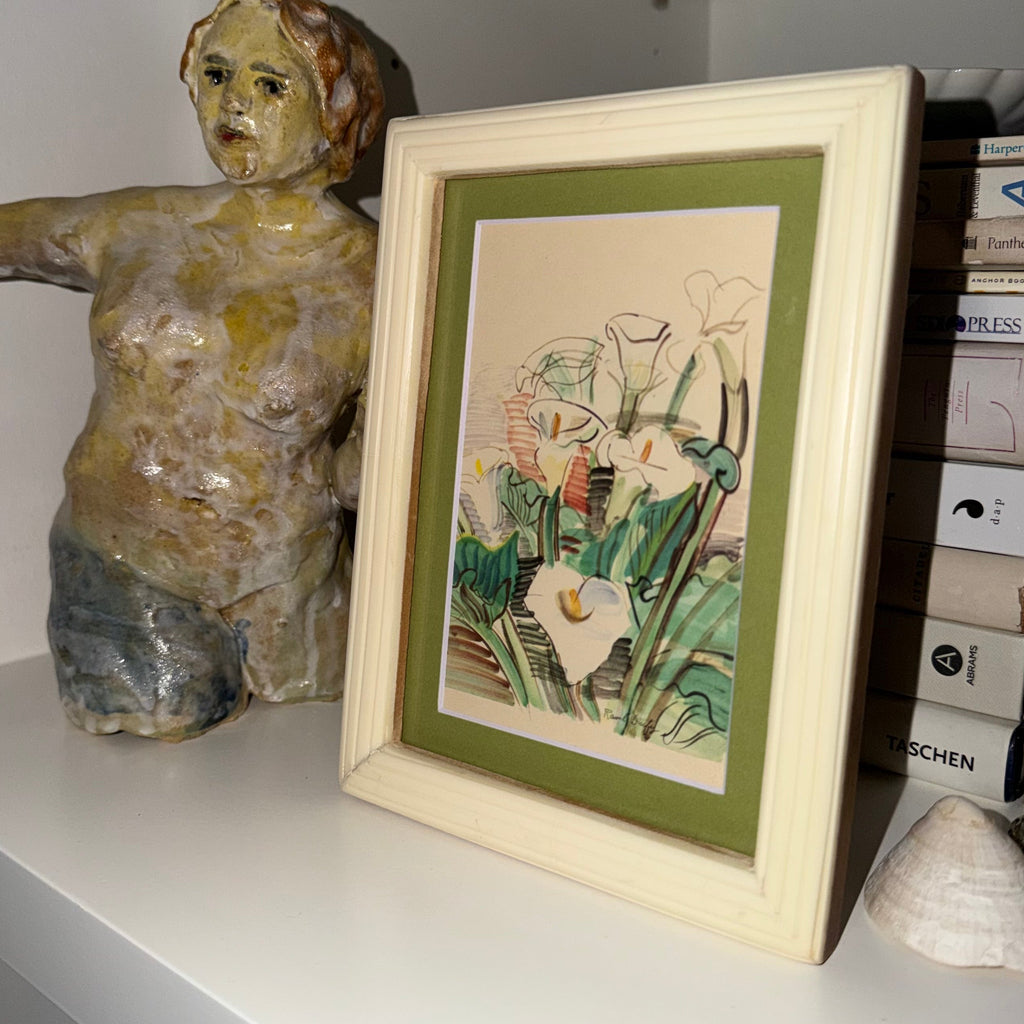 Framed artwork of flowers on a shelf with a ceramic figure and books.