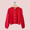 Red cardigan on a wooden hanger against a white background