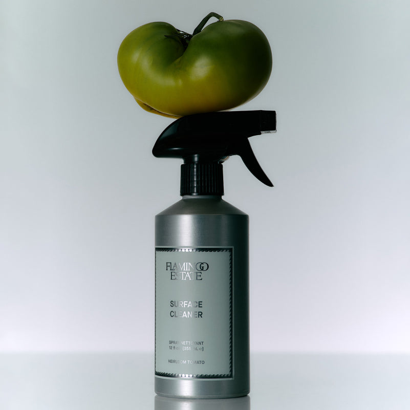 Spray bottle labeled 'Flamingo Estate' with a green tomato on top against a white background
