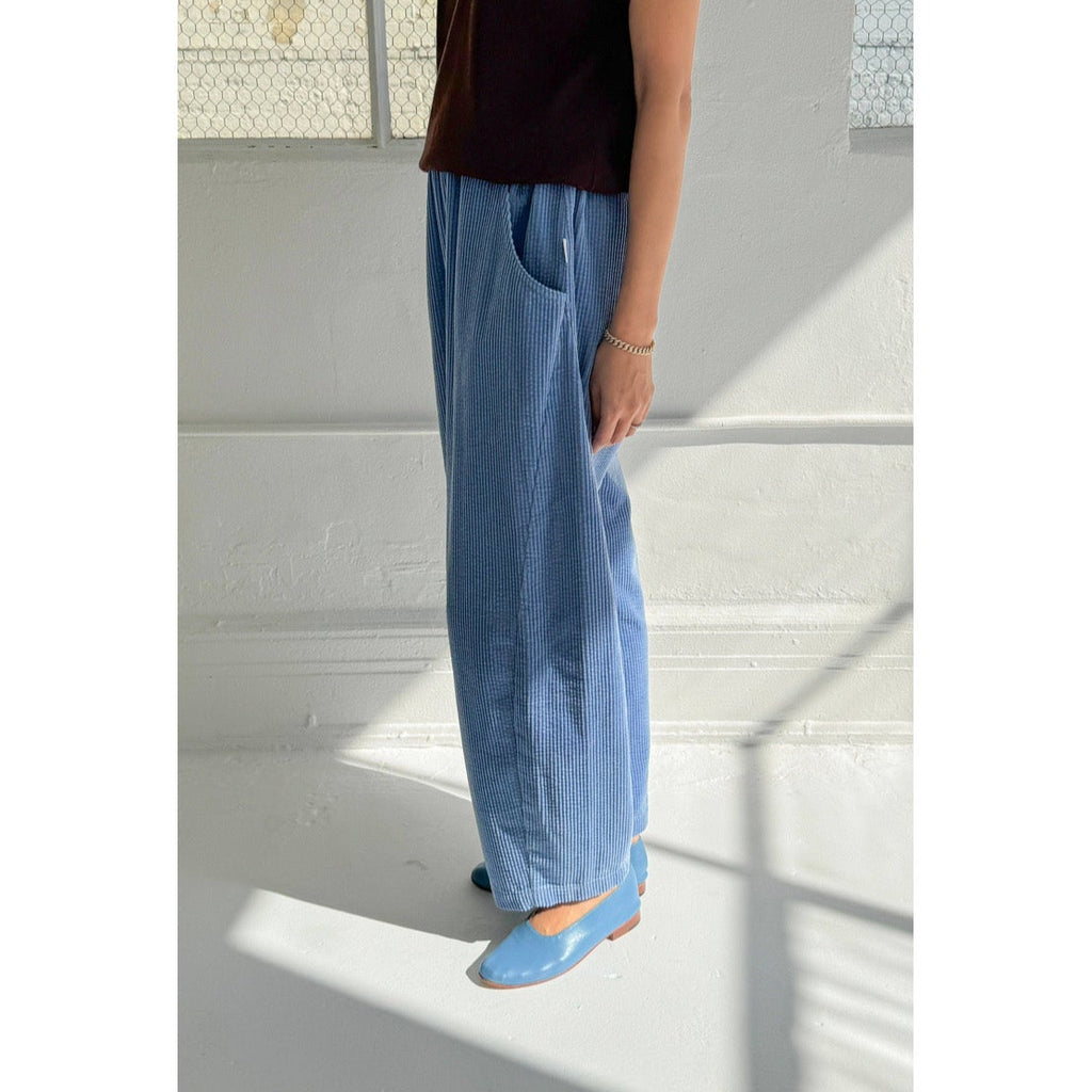 Person wearing blue Le Bon Shoppe pants and blue shoes standing on a white floor with a light gray wall.