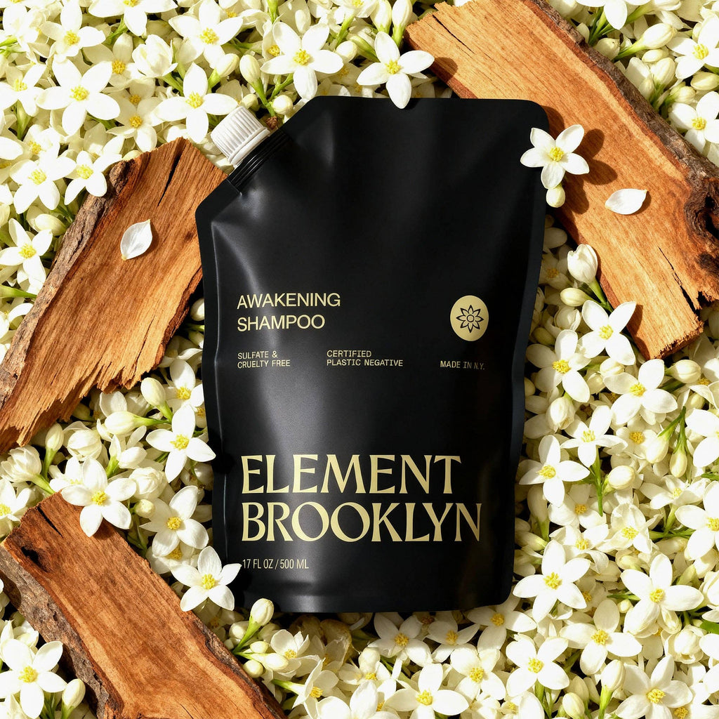 Element Brooklyn shampoo pouch surrounded by white flowers and wooden logs