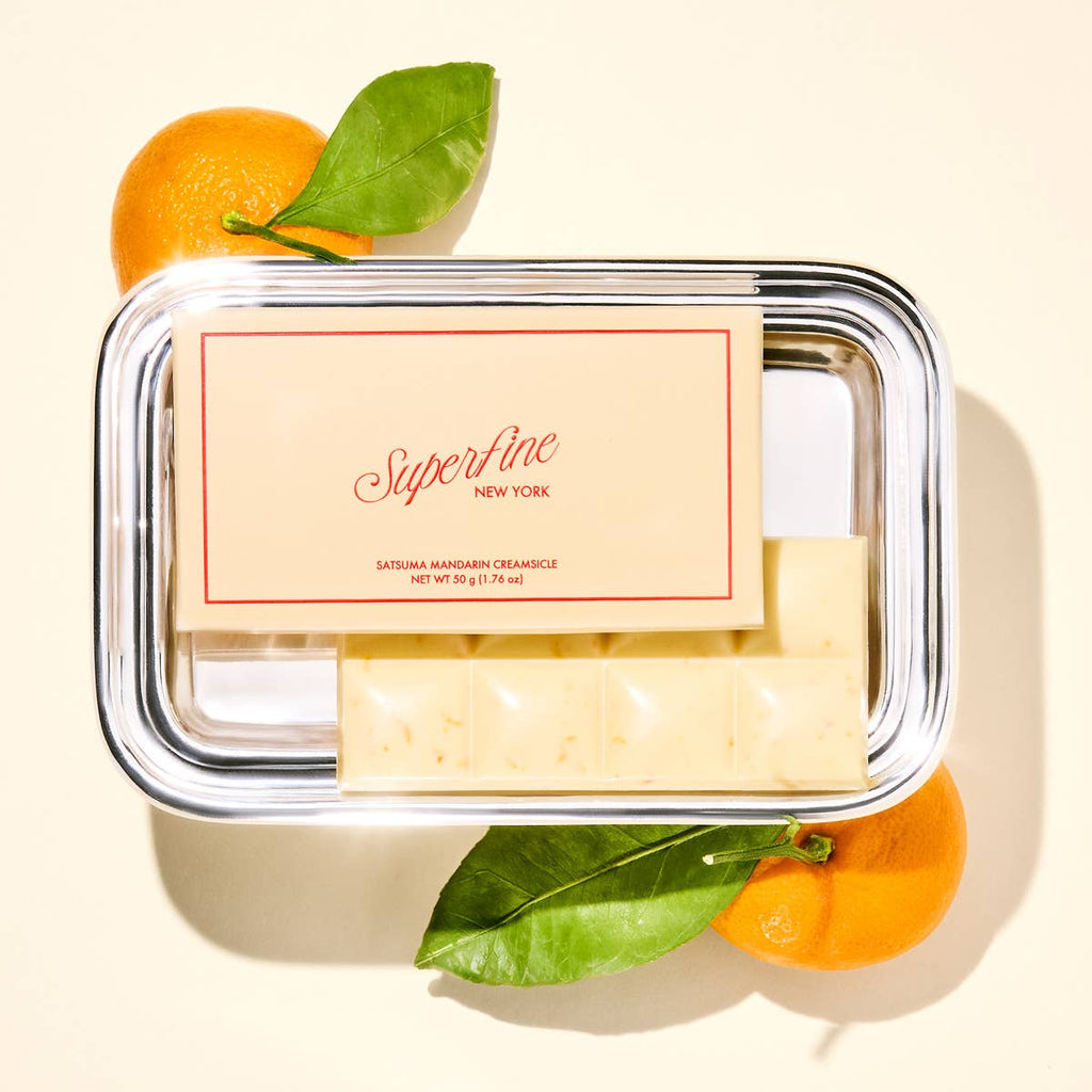 Handmade chocolate bar on a platter with 'Superfine New York' label, surrounded by satsuma mandarin oranges on a light background.