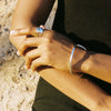 Close-up of a person's arm with Moneh Brisel hand carved jewelry against a natural background