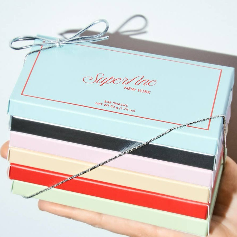Hand holding a colorful box with 'Superfine New York' branding on a light background
