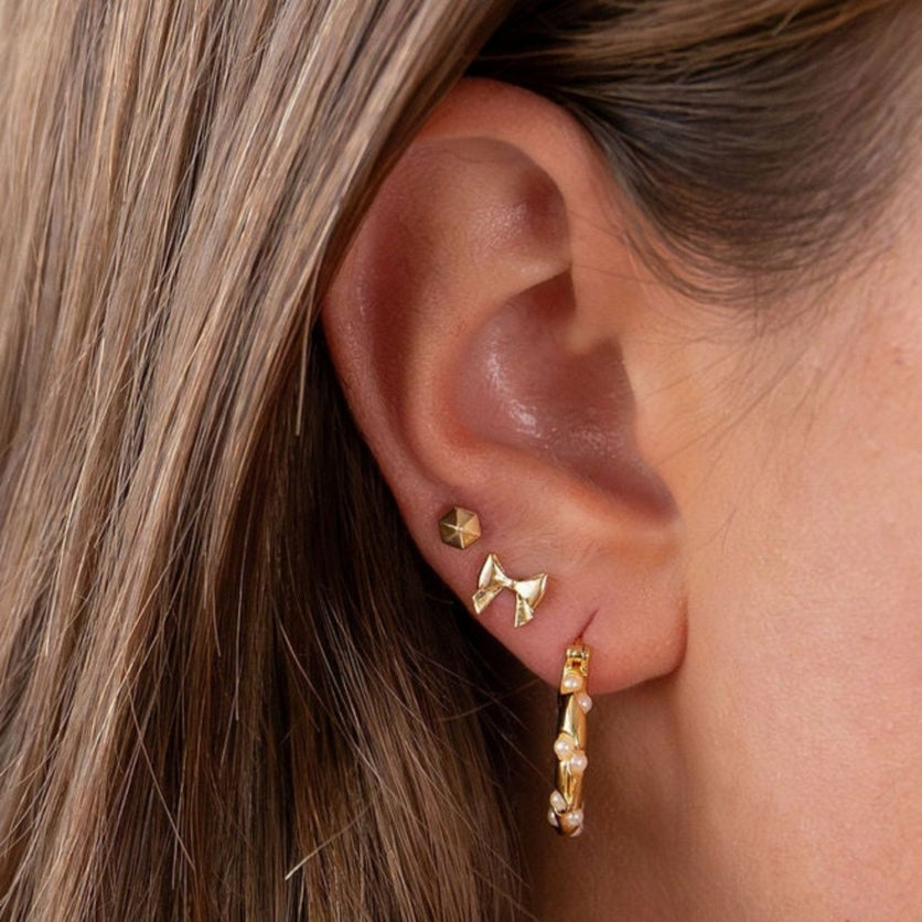 Close-up of an ear wearing bow earrings with a blurred background