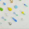 A variety of vintage glass and enamel charms in different colors with gold or silver rings, displayed on a white surface.
