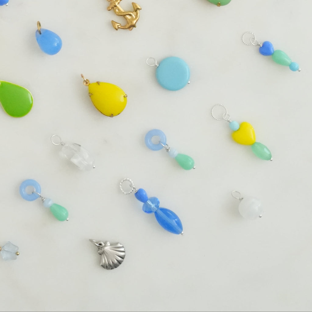 A variety of vintage glass and enamel charms in different colors with gold or silver rings, displayed on a white surface.