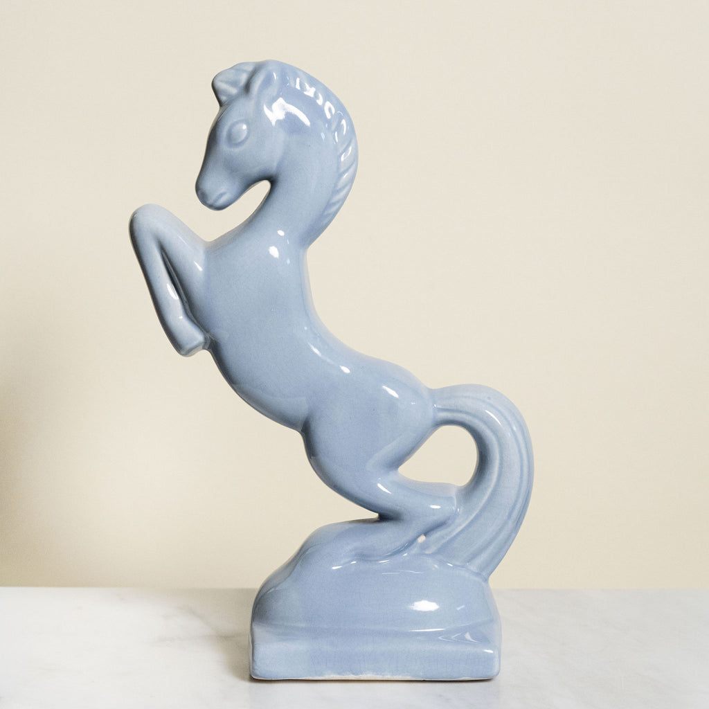 Vintage blue ceramic horse sculpture on a white surface with a beige background