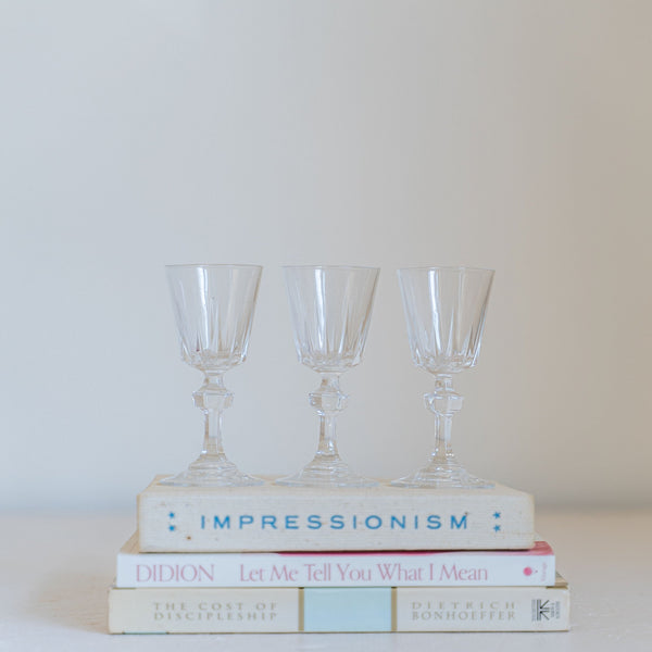 Vintage crystal cordial drink glasses in a row of three stacked atop a pile of vintage books.