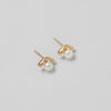 Gold earrings with pearl studs on a light gray background
