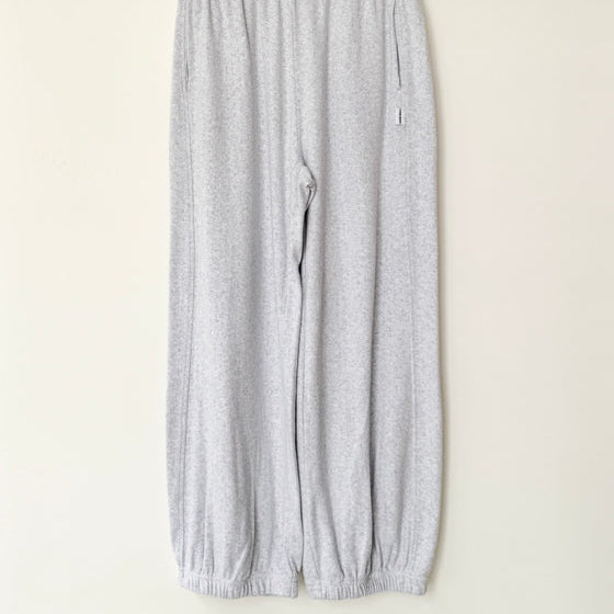 Gray sweatpants hanging on a wooden hanger against a white wall