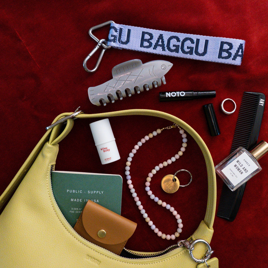 Yellow handbag with various items on a red background, including a baggu keychain lanyard.