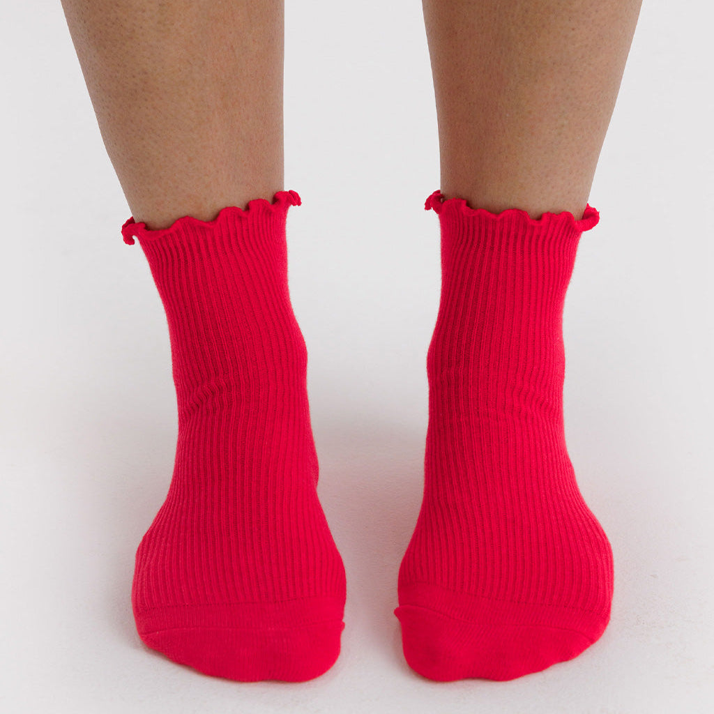 Red socks with ruffled top worn by a person on a white background by Baggu