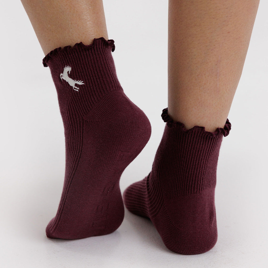 Maroon socks with ruffled top and small horse worn by a person on a white background