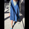 Person wearing a blue denim dress over a striped shirt on a street.