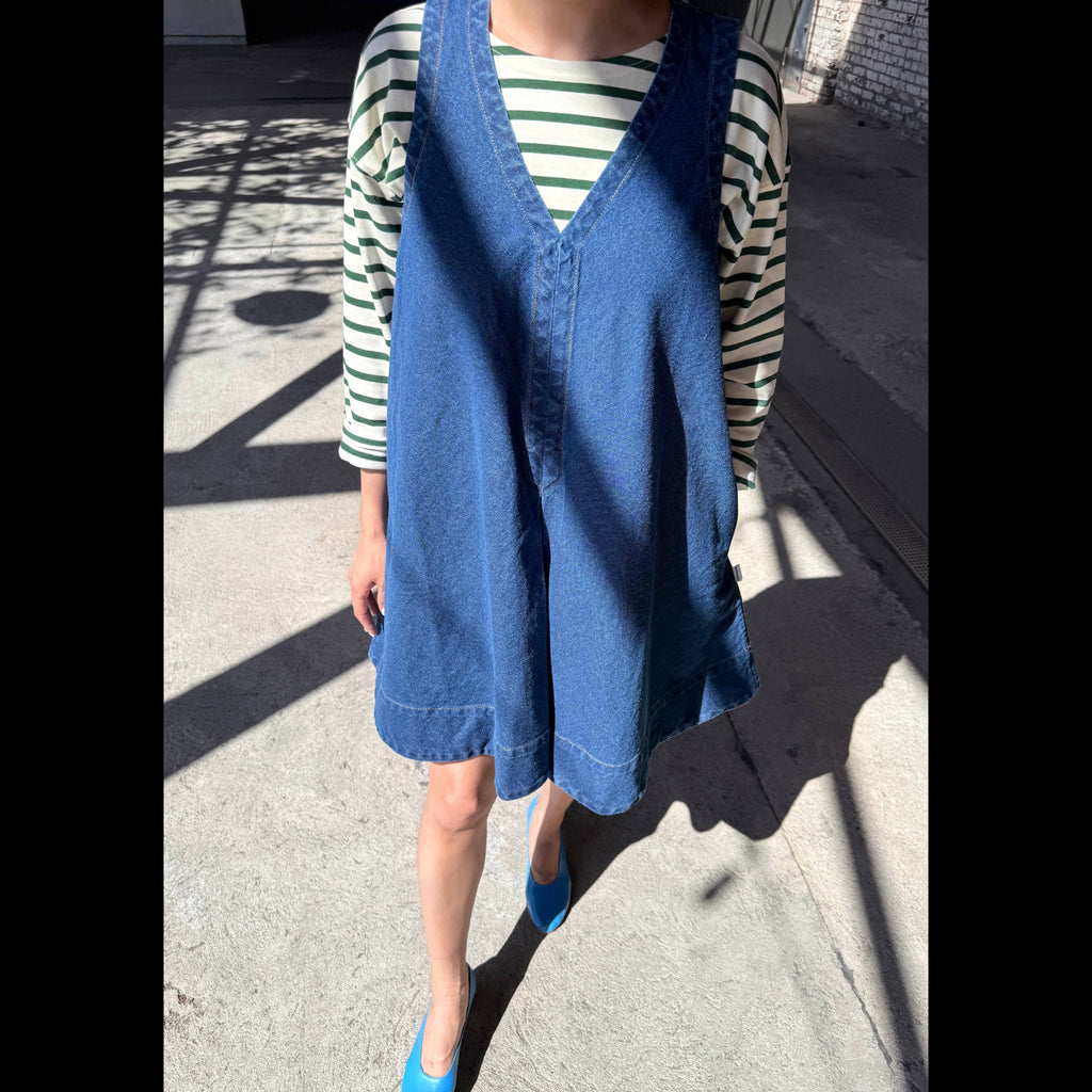 Person wearing a blue denim dress over a striped shirt on a street.