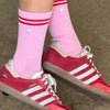 Red Adidas sneakers with white stripes worn with pink socks on a concrete floor.