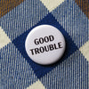 Button with 'Good Trouble' text on a checkered fabric background