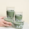 Set of green glass tumblers with white patterns on a light background