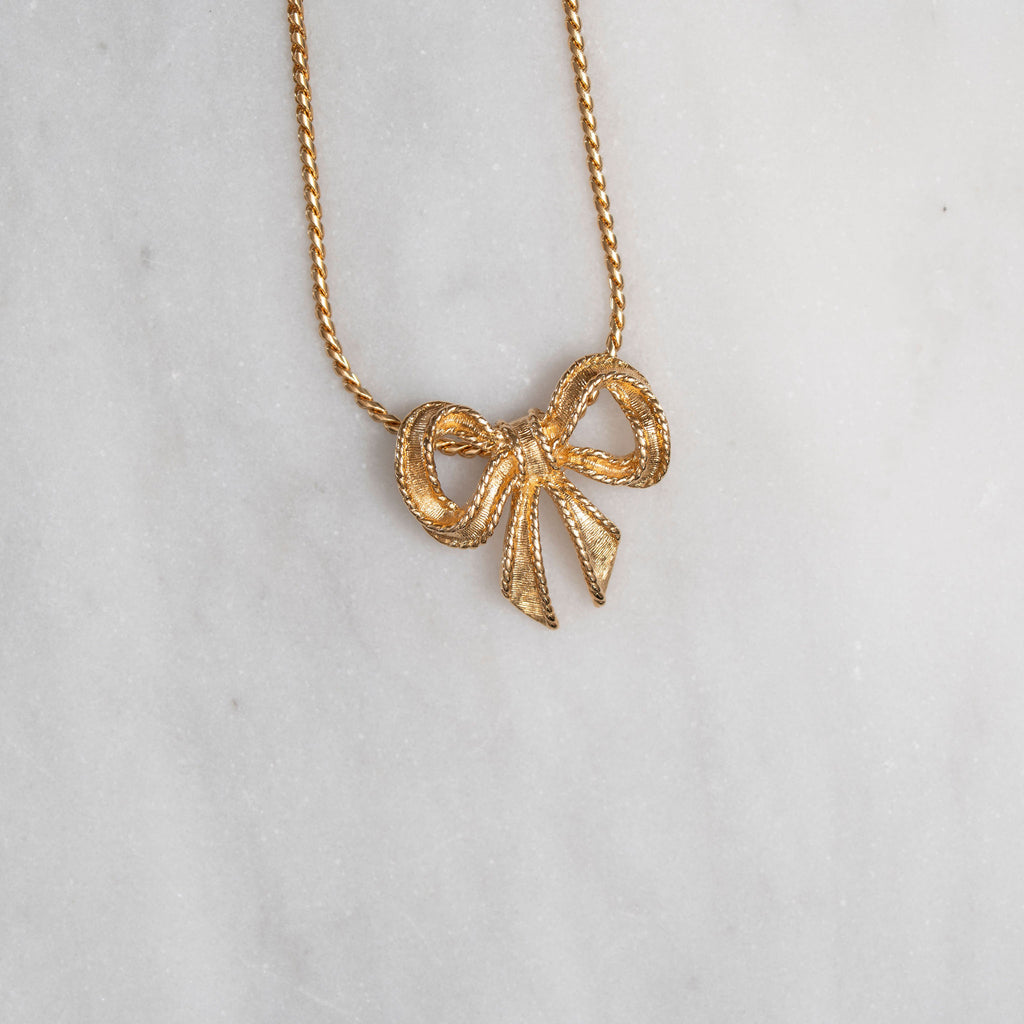 Gold bow-shaped pendant necklace on a light gray background