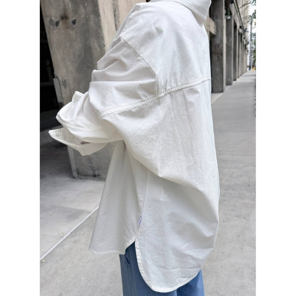 White oversized shirt worn by a person on a city street.