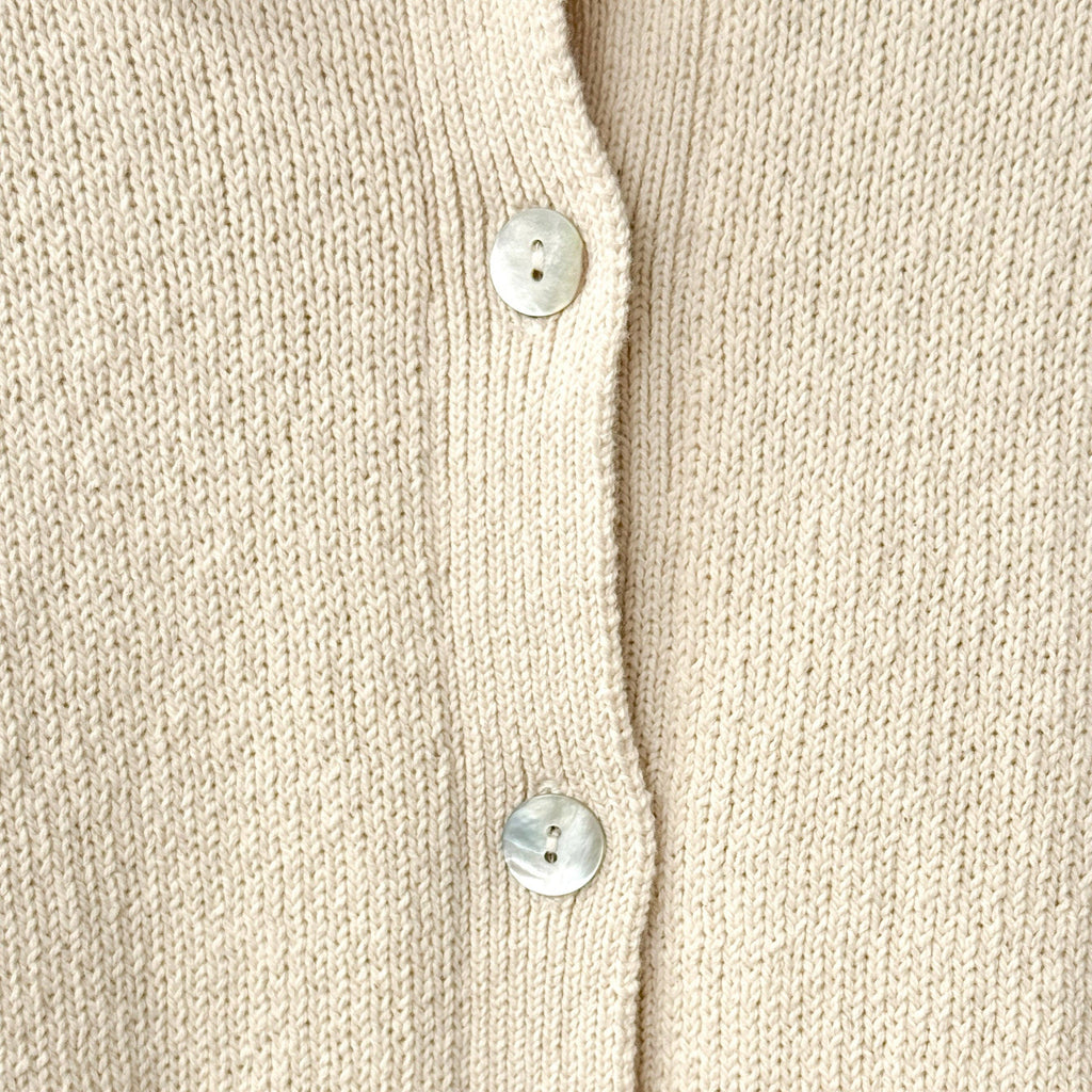 Close-up of a beige cardigan with shell buttons on a beige background