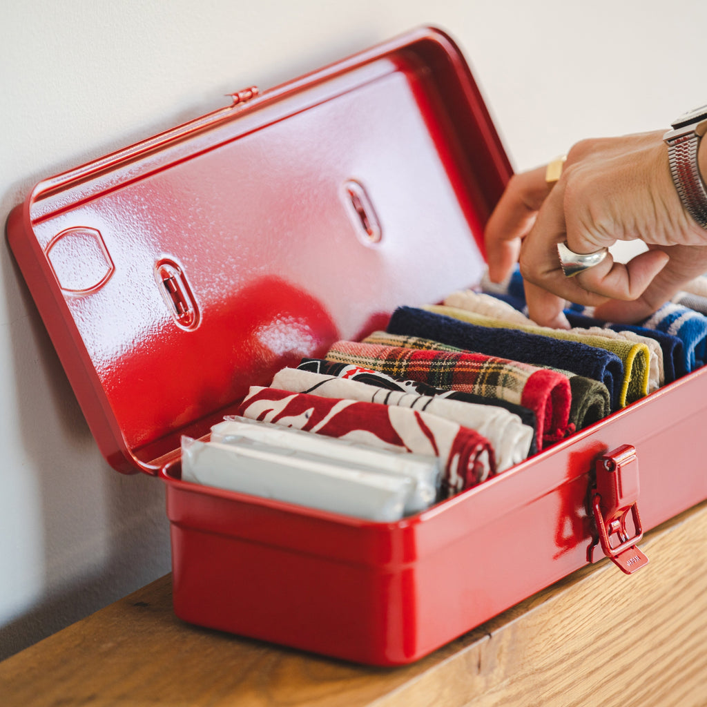 Red metal box with neatly folded clothes on a wooden surface